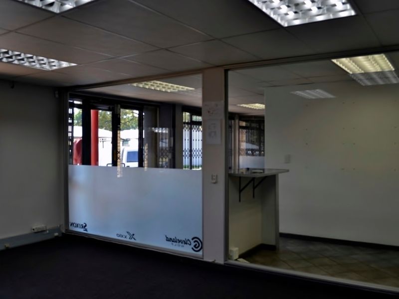An empty office space featuring glass partitions, suspended ceilings with recessed lighting, and a built-in counter area, suitable for professional use.