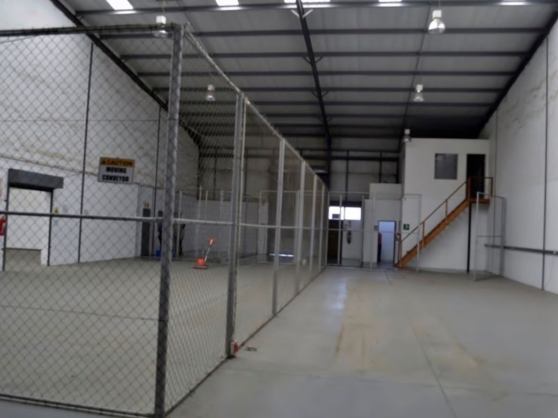 Spacious industrial warehouse unit featuring high ceilings, concrete flooring, a mezzanine level with staircase access, and partitioned chain-link fenced areas.