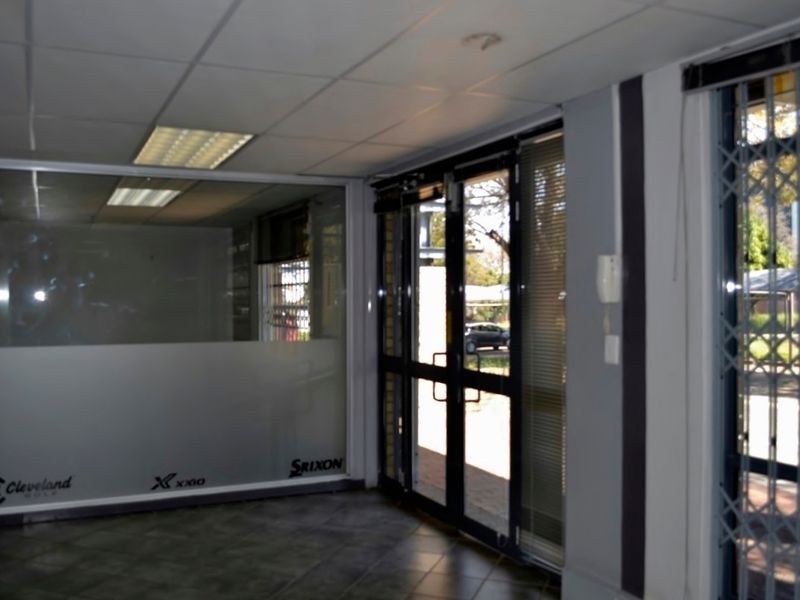 A bright industrial entry area featuring tiled flooring, a suspended ceiling, glass partitioning, and secure aluminium-framed glass doors with security gates.