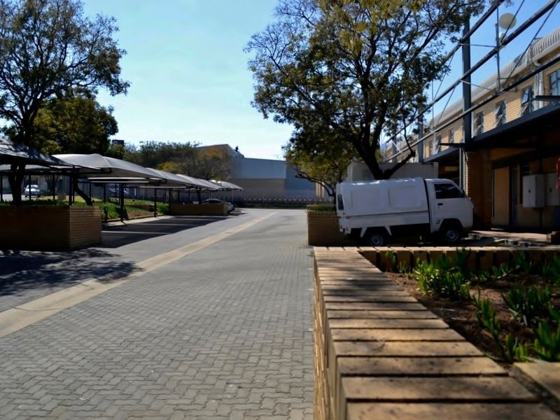 Industrial property exterior featuring a paved driveway with covered parking bays, brick retaining walls, and established trees.