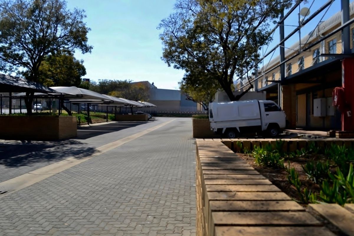 Industrial property exterior featuring a paved driveway with covered parking bays, brick retaining walls, and established trees.