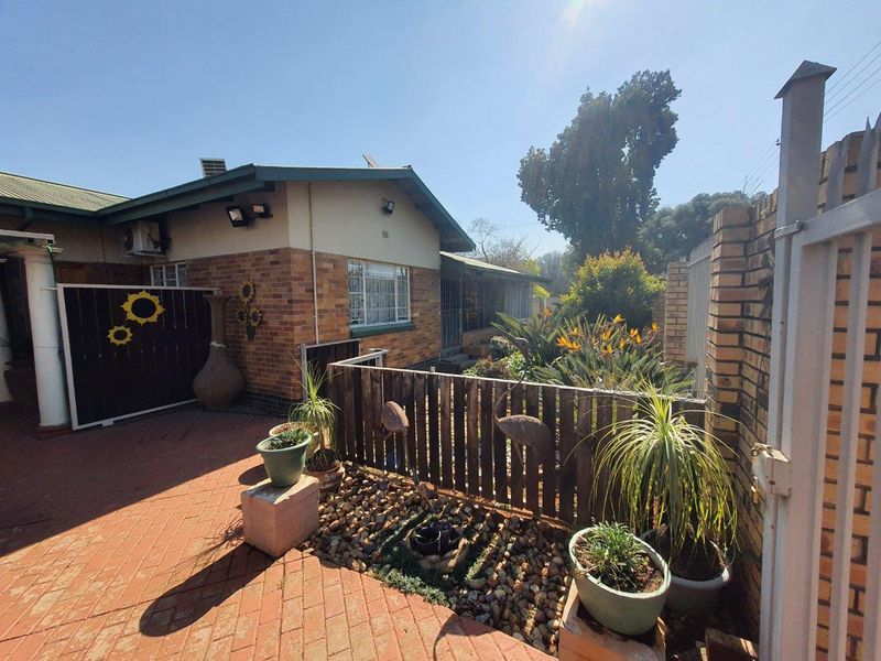 A rear exterior view of the house featuring a brick facade, paved patio area, and enclosed garden space with a timber fence and security gate.