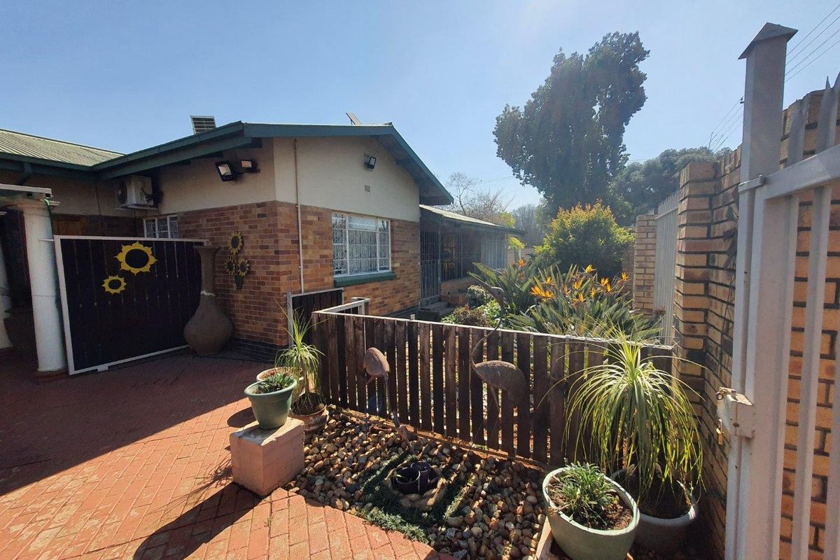 A rear exterior view of the house featuring a brick facade, paved patio area, and enclosed garden space with a timber fence and security gate.