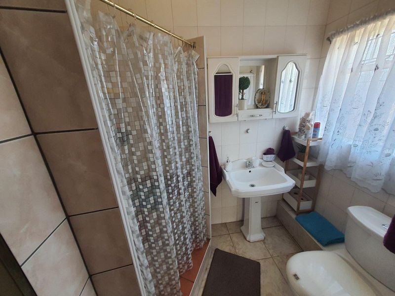 A functional bathroom featuring a pedestal basin, shower enclosure, and tiled finishes, offering a practical layout with potential for modern updates.
