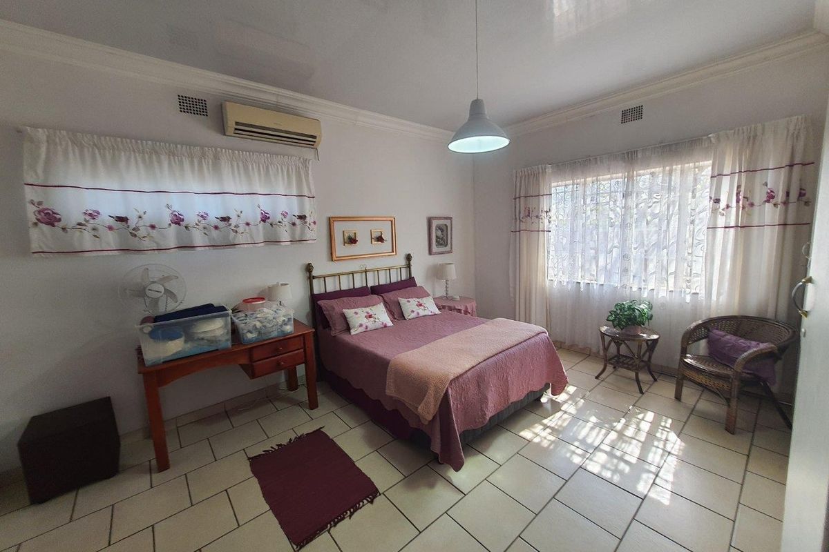 Spacious bedroom featuring tiled flooring, air conditioning, and large windows with security bars, offering a functional and well-lit living space.