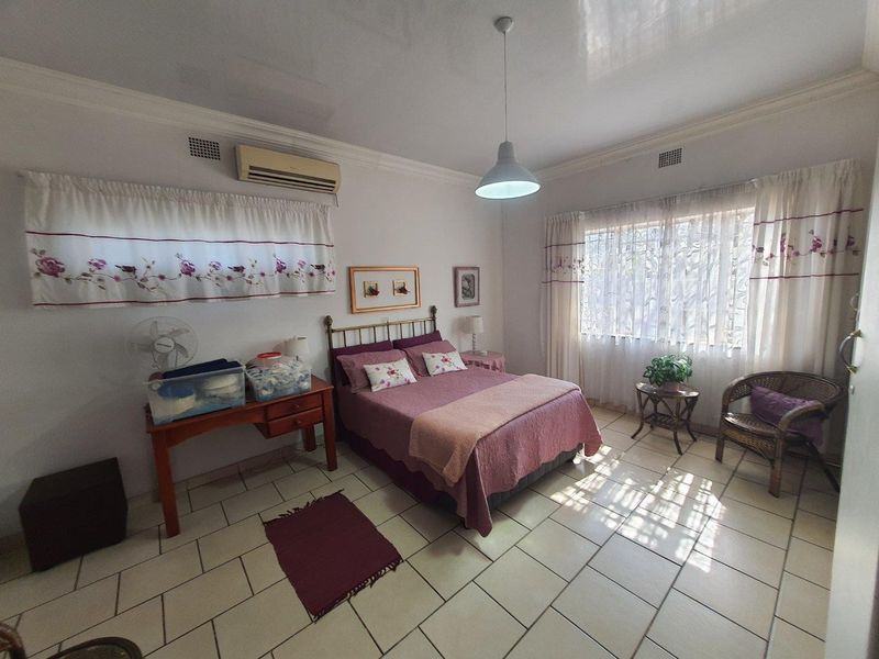 Spacious bedroom featuring tiled flooring, air conditioning, and large windows with security bars, offering a functional and well-lit living space.
