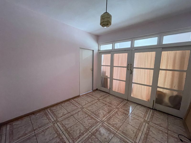 An empty living room featuring tiled flooring, a pendant light, and large glass-panelled double doors with transom windows providing natural light.