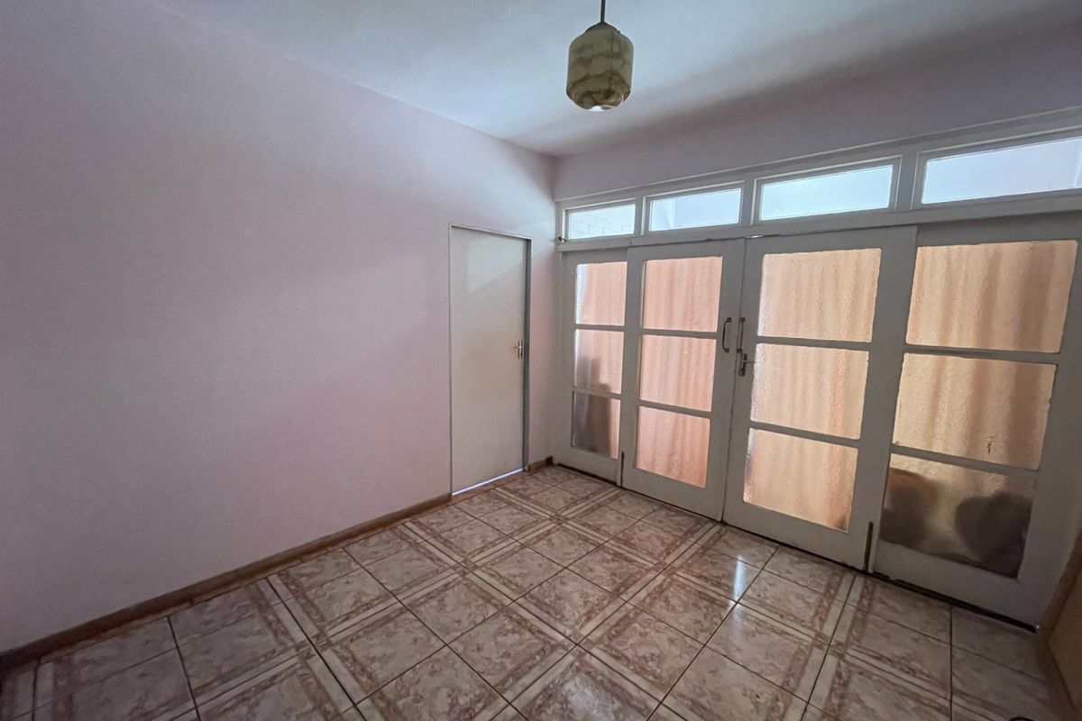 An empty living room featuring tiled flooring, a pendant light, and large glass-panelled double doors with transom windows providing natural light.