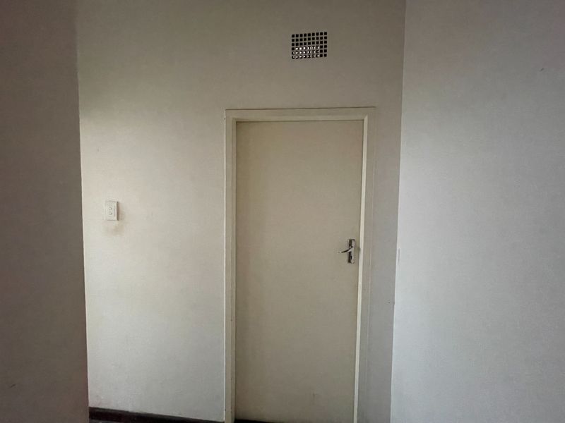 A simple interior hallway featuring a standard door, ventilation grille, and electrical light switch on a plain wall.