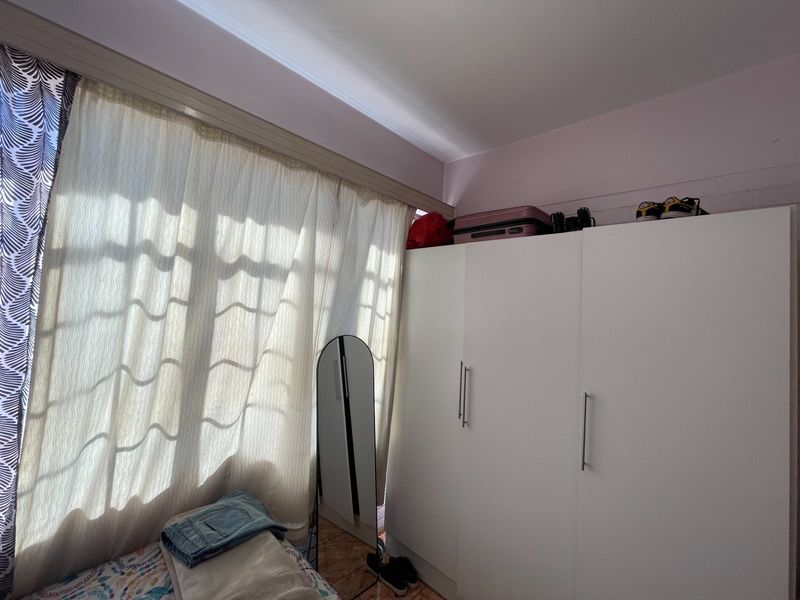 A bedroom featuring a white built-in wardrobe and large window with curtain rail, providing natural light and storage space.