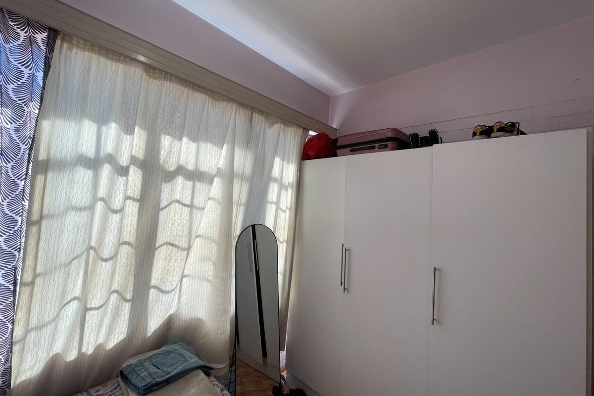 A bedroom featuring a white built-in wardrobe and large window with curtain rail, providing natural light and storage space.