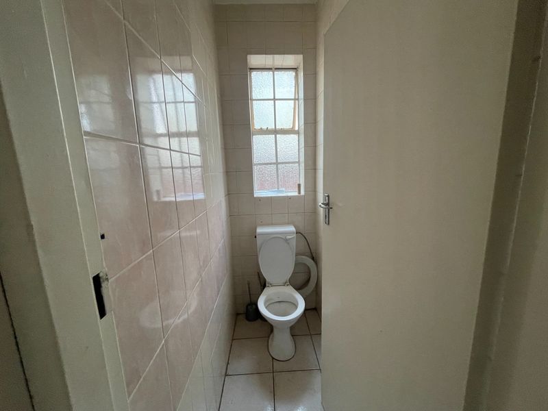 A compact, dated guest toilet featuring ceramic wall and floor tiles and a small window.