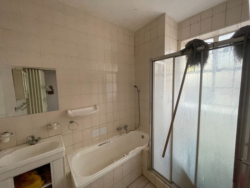 A dated bathroom featuring a bathtub, shower enclosure, and vanity basin, requiring modernization of finishes and fixtures.