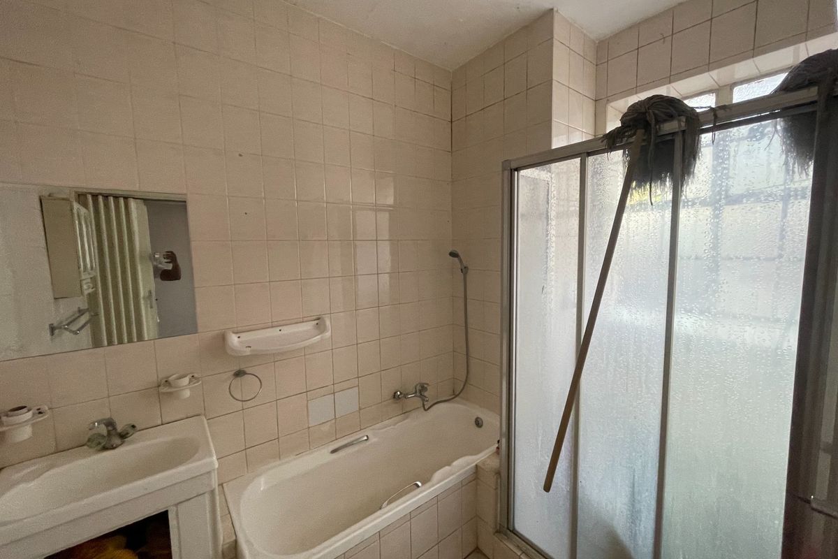 A dated bathroom featuring a bathtub, shower enclosure, and vanity basin, requiring modernization of finishes and fixtures.