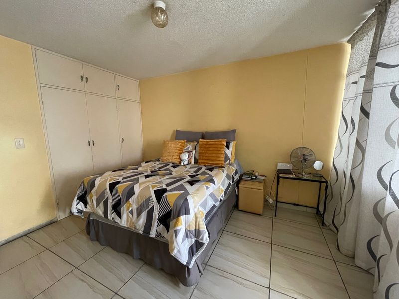 A bedroom featuring built-in cupboards, tiled flooring, and a ceiling light fixture, requiring cosmetic updates to the wall finishes.