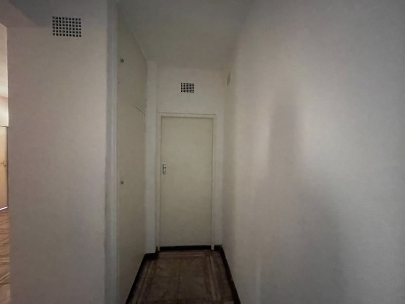 A simple, empty hallway featuring tiled flooring, a built-in storage cupboard, and ventilation grilles, requiring minor cosmetic updates to refresh the space.