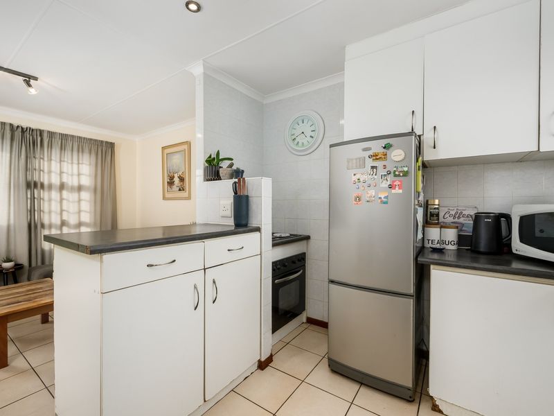Compact kitchen featuring white cabinetry, dark laminate countertops, tiled backsplash, and built-in oven, with an adjacent breakfast bar area.