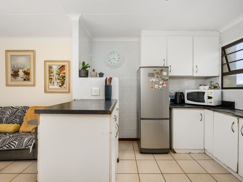 Open-plan kitchen area featuring white cabinetry, dark laminate countertops, tiled flooring, and a breakfast bar connecting to the adjacent living space.