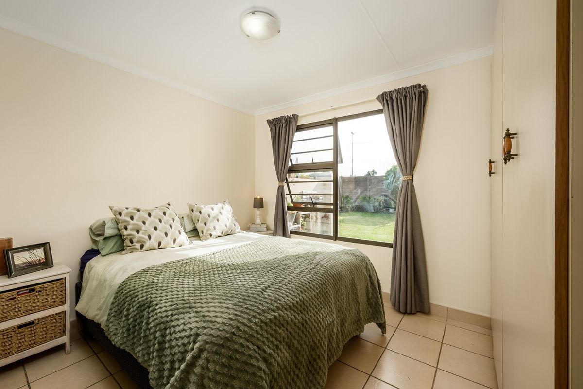 A functional bedroom featuring tiled flooring, built-in cupboards, and a window overlooking the rear garden area.