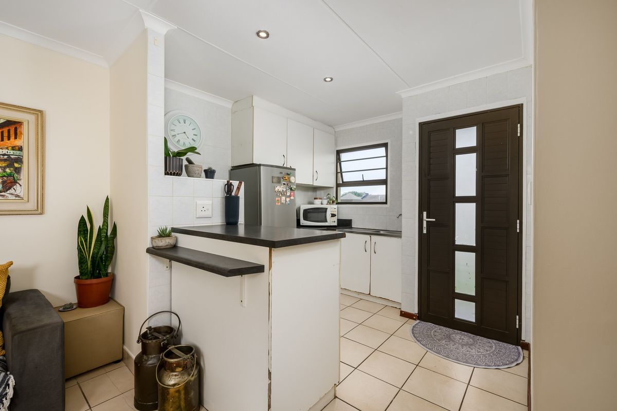 Compact kitchen featuring white cabinetry, dark laminate countertops, a breakfast bar, tiled flooring, and direct access to an exterior door.