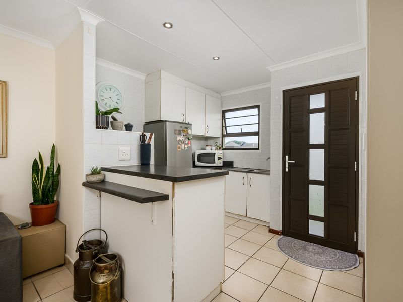 Compact kitchen featuring white cabinetry, dark laminate countertops, a breakfast bar, tiled flooring, and direct access to an exterior door.