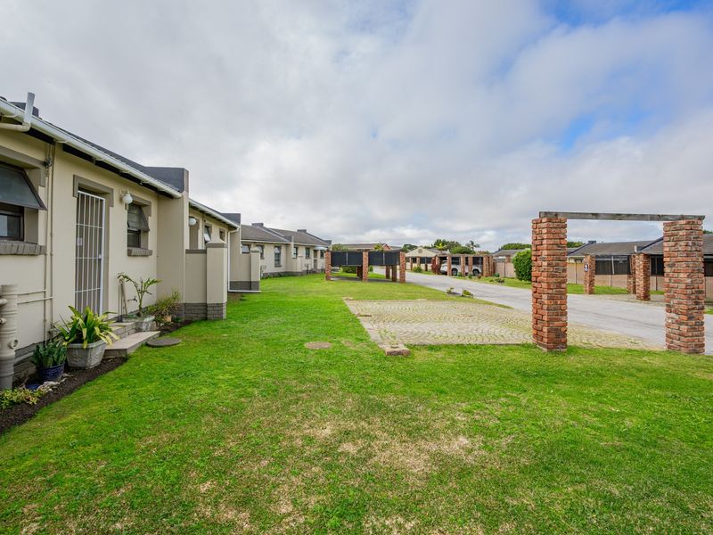 A view of the rear exterior area featuring a well-maintained lawn, paved driveway, and brick structural pillars.
