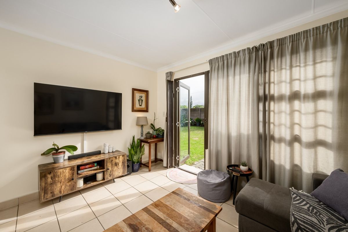 A bright living room featuring tiled flooring and a glass sliding door providing direct access to the rear garden.