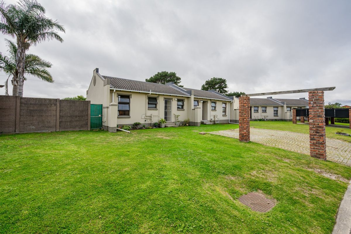 Rear view of the property featuring a spacious lawn, paved driveway area, brick boundary wall, and a tiled roof structure.