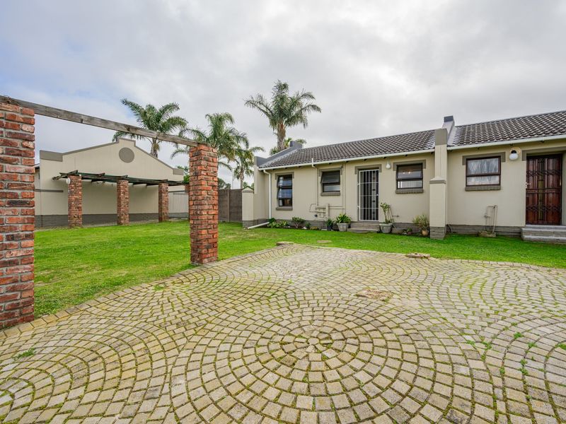 Rear view of the property featuring a brick-paved courtyard, a brick pergola structure, and a well-maintained lawn area.