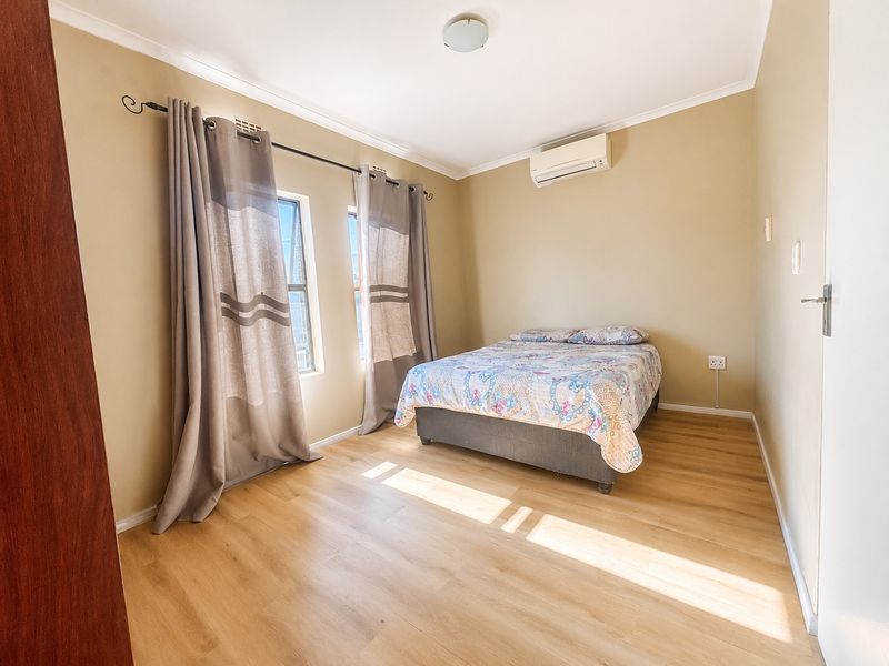 A well-lit bedroom featuring light-toned laminate flooring, a wall-mounted split-system air conditioner, and neutral wall finishes.