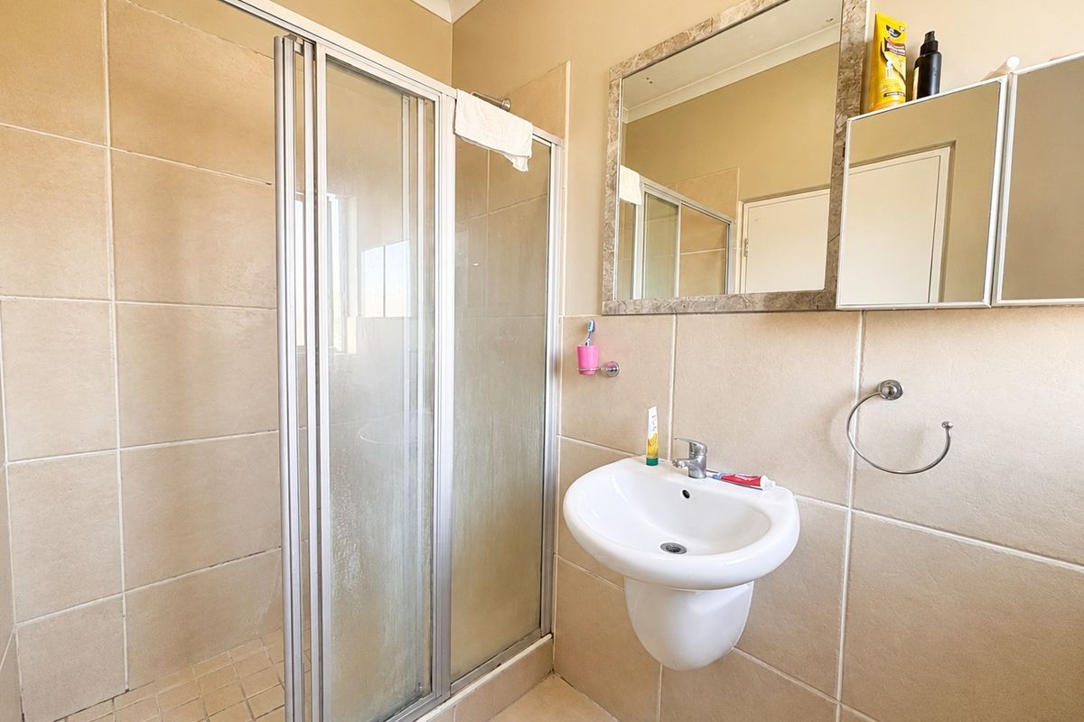 A functional bathroom featuring a tiled shower enclosure, wall-mounted basin, and neutral wall tiling, offering a clean and practical space.
