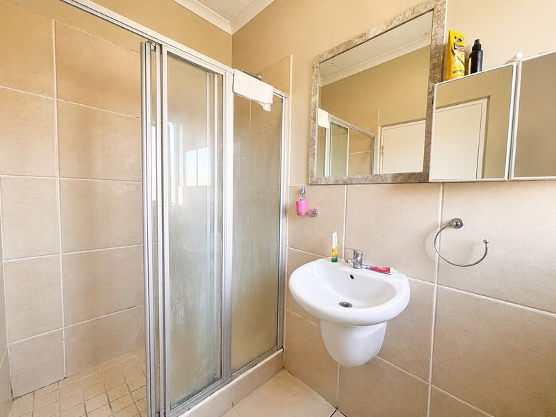 A functional bathroom featuring a tiled shower enclosure, wall-mounted basin, and neutral wall tiling, offering a clean and practical space.
