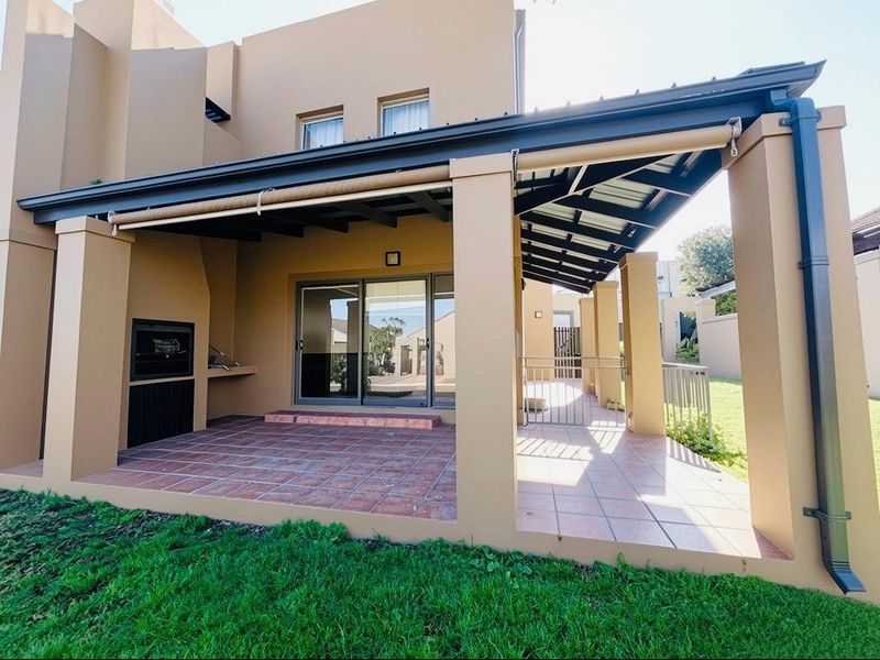 A spacious covered patio featuring tiled flooring, a built-in braai, and direct access to the interior through sliding glass doors.