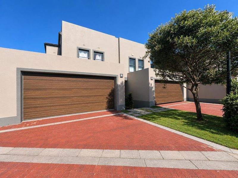 Modern double-storey residential facade featuring a double garage, paved driveway, and well-maintained front garden area.