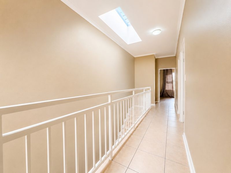 A bright, tiled upper-level hallway featuring a skylight and a white metal balustrade overlooking the staircase.