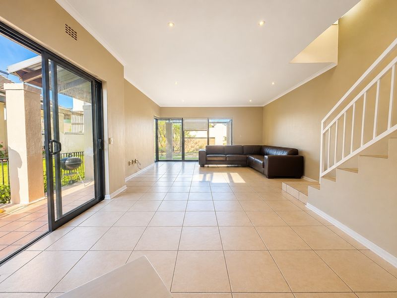 Spacious open-plan living area featuring neutral tiled flooring, recessed lighting, and large sliding glass doors providing access to the outdoor patio area.