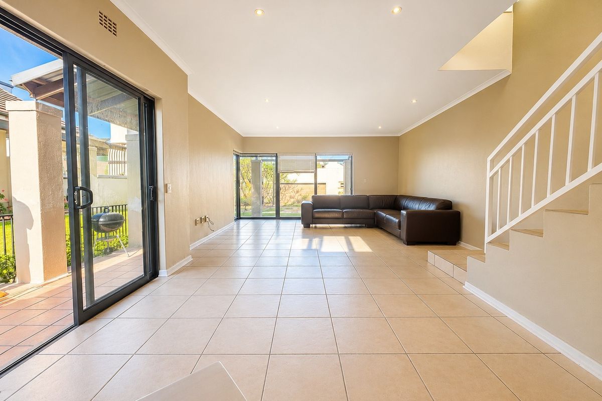 Spacious open-plan living area featuring neutral tiled flooring, recessed lighting, and large sliding glass doors providing access to the outdoor patio area.