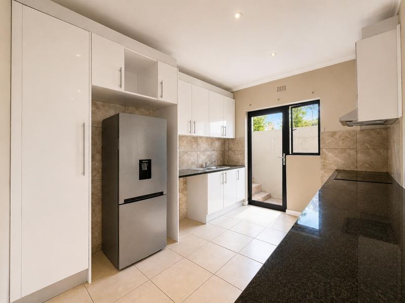Modern kitchen featuring white cabinetry, dark granite countertops, tiled backsplash, and direct access to an outdoor area through a glass panel door.