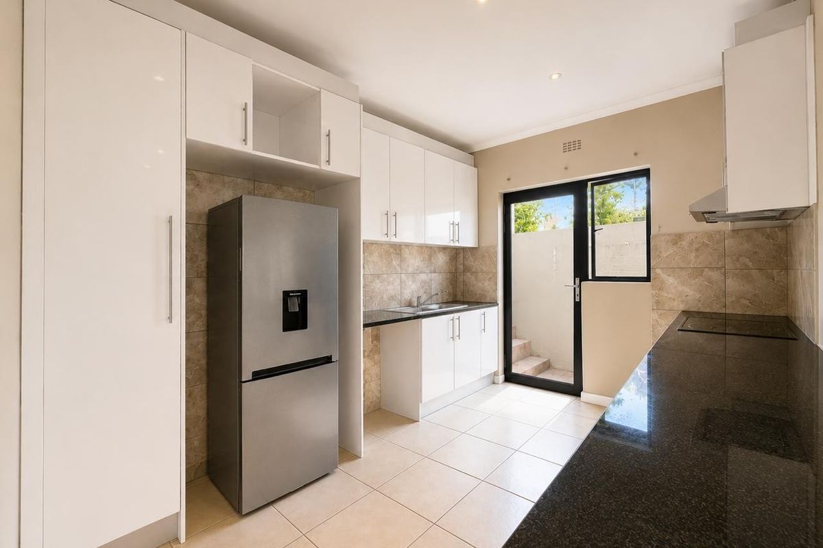 Modern kitchen featuring white cabinetry, dark granite countertops, tiled backsplash, and direct access to an outdoor area through a glass panel door.