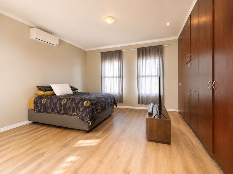 A well-maintained bedroom featuring laminate flooring, extensive floor-to-ceiling built-in cupboards, and a wall-mounted split-system air conditioner for climate control.