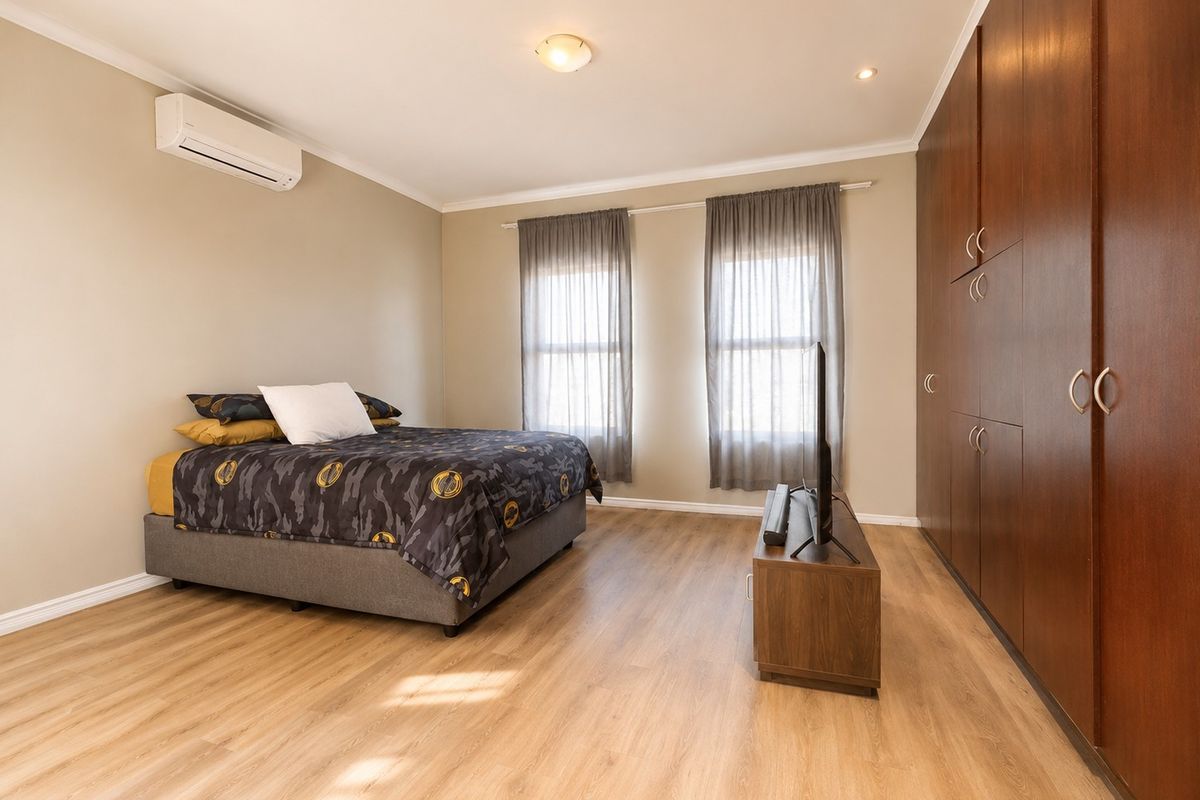 A well-maintained bedroom featuring laminate flooring, extensive floor-to-ceiling built-in cupboards, and a wall-mounted split-system air conditioner for climate control.