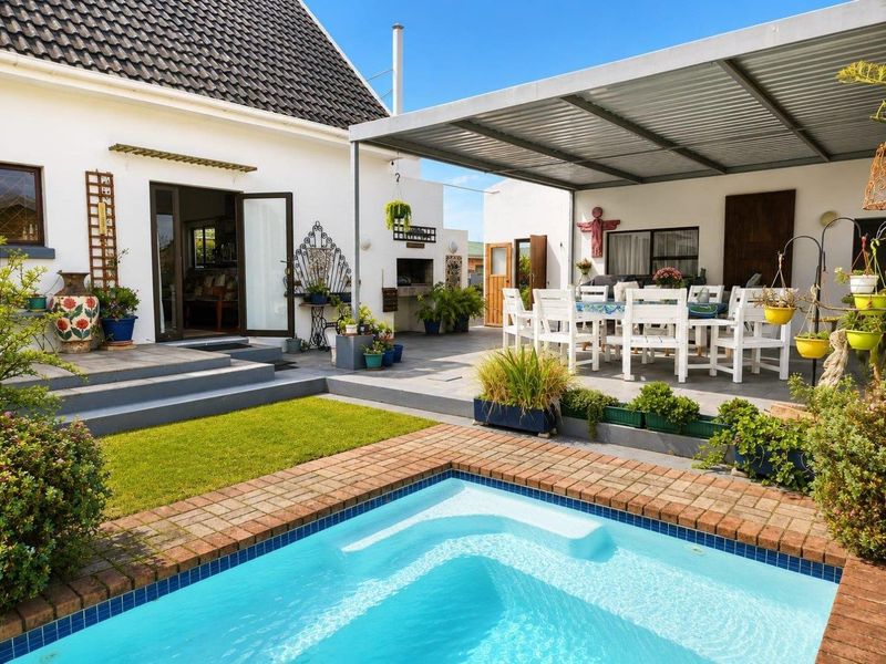 Outdoor entertainment area featuring a swimming pool with brick coping, a covered patio with tiled flooring, and a built-in braai facility.