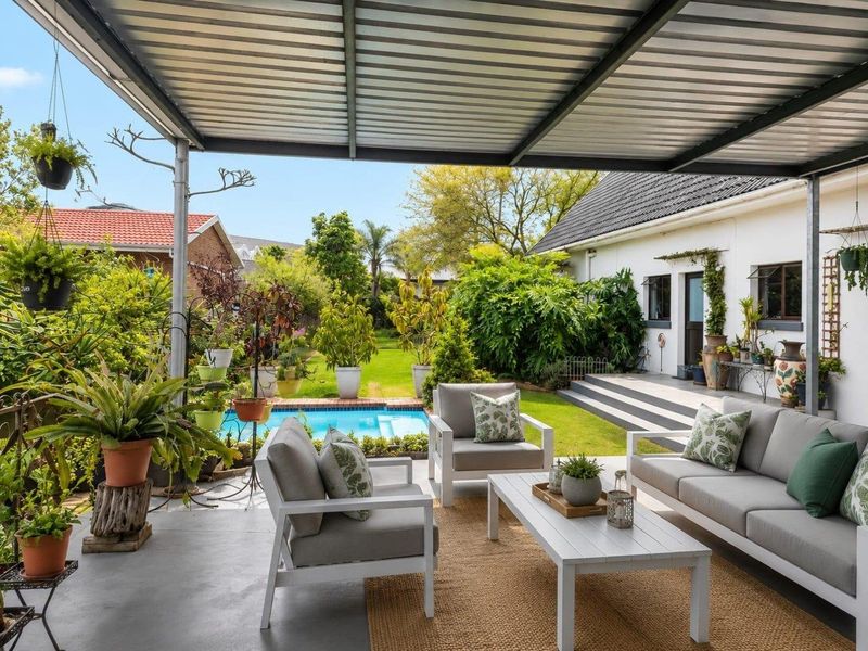 Covered outdoor patio area featuring a metal roof, overlooking a private swimming pool and well-maintained garden space.