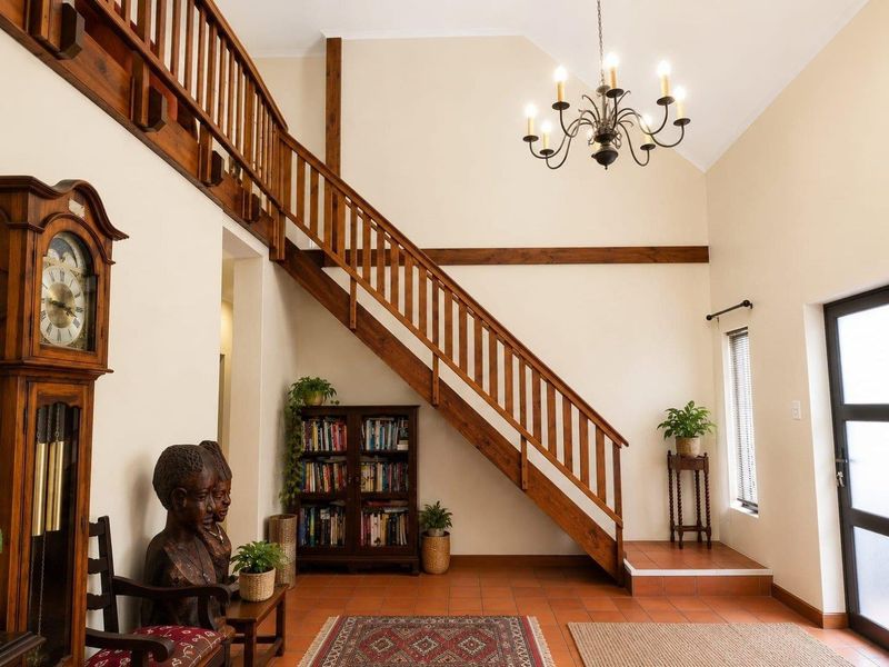 Spacious entrance hall featuring a vaulted ceiling, exposed wooden beams, a classic wooden staircase with balustrade, and durable terracotta floor tiles.
