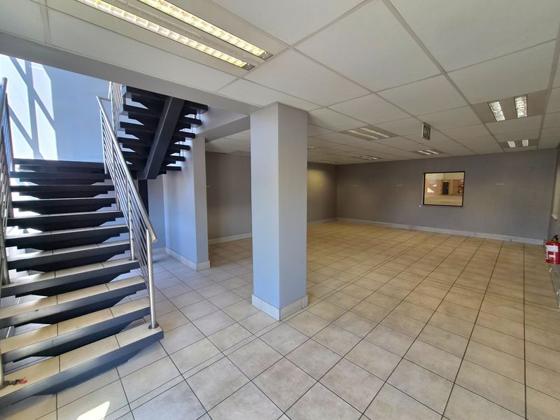 Spacious open-plan industrial office or showroom area featuring ceramic tiled flooring, a modern metal staircase, and recessed ceiling lighting.