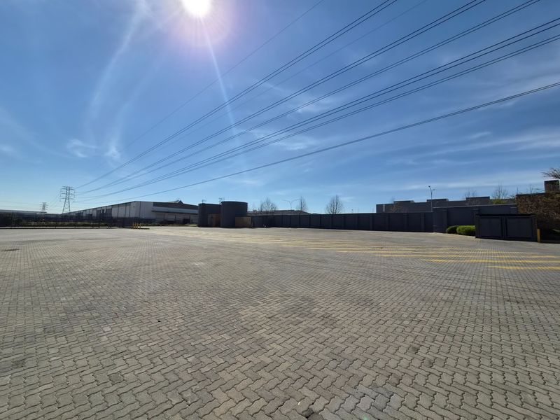 Spacious paved industrial yard area featuring a secure perimeter wall, gated access, and clearly marked parking bays.