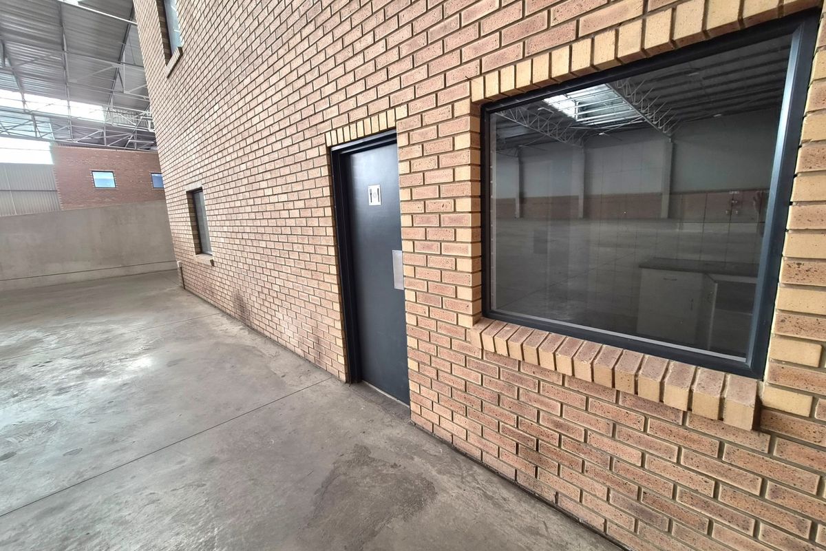 Exterior view of an industrial property featuring a face brick facade, concrete flooring, and metal door access within a large warehouse structure.