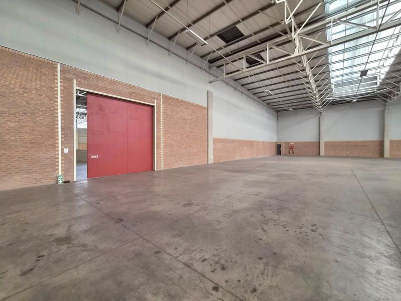 Spacious industrial warehouse unit featuring high ceilings with exposed steel trusses, skylights for natural light, concrete flooring, and a large industrial sliding door.