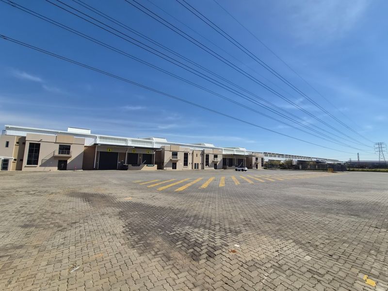 Wide-angle view of an industrial facility featuring multiple loading bays, roller shutter doors, and a large paved yard area.