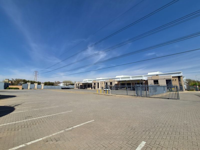 Wide-angle view of an industrial property featuring a large paved parking area, secure metal fencing, and multiple warehouse loading bays.